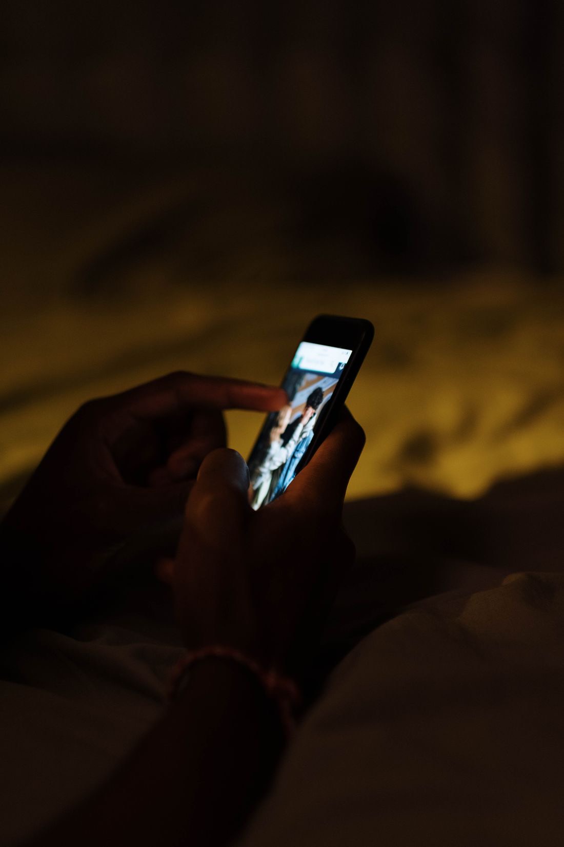 Hands holding a phone lit up in a dark room at night.